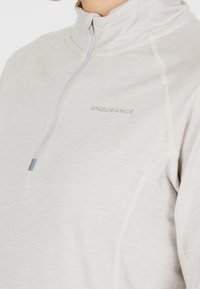 Light grey zip-up jacket with high collar, soft texture, contrasting seams, and "ENDURANCE" logo printed on the chest.