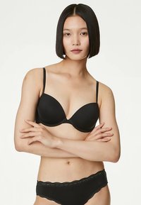 Sujetador negro acolchado con tirantes delgados, caracterizado por una textura suave y copas redondeadas. Combinado con braguitas negras a juego adornadas con encaje.