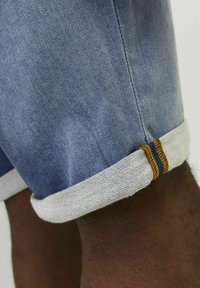 Bermudas de mezclilla con un corte ajustado, en un color azul claro, con dobladillos enrollados en un tono más claro, y detalles de costura en naranja y marino que contrastan.