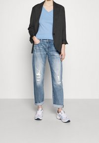 Överdimensionerad grå kavaj med ränder över en blå v-ringad topp, kombinerad med bleka blå slitna jeans och vita sneakers.