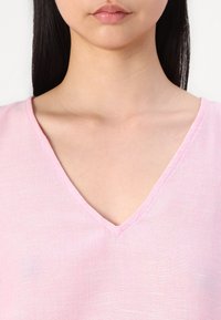 Top a V scollo in lino rosa soft, con un tessuto texturizzato, cuciture sottili lungo il collo e una vestibilità morbida attorno al colletto.