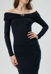 Dunkelmarinefarbenes schulterfreies Kleid mit langen Ärmeln, mit einem drapierten Ausschnitt und einem goldenen Akzent in der Mitte. Schmale Passform mit strukturiertem Stoff.