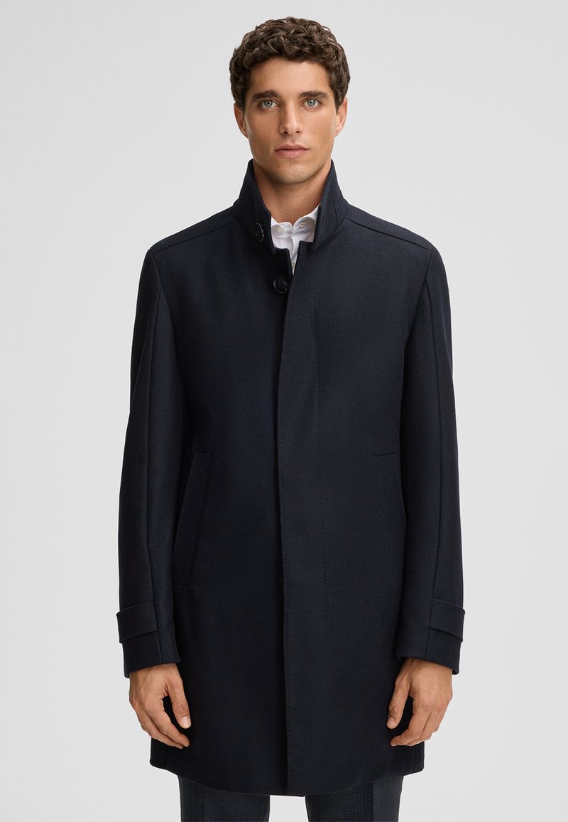 Marineblauwe wolblend jas met een hoge kraag, zijzakken en een enkele knoopsluiting. Glad textuur en een getailleerde pasvorm.