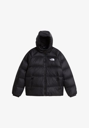 Noor inimene, kes kannab musta peapaela, musta kapuutsiga sulejopet ja musta pükse, kõigil The North Face'i logo, käed jope taskutes.