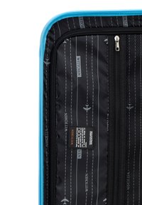 Interno della valigia Wittchen con tessuto nero decorato con motivi di aeroplani e linee bianche, zipper blu e un'etichetta del marchio con istruzioni per la cura.