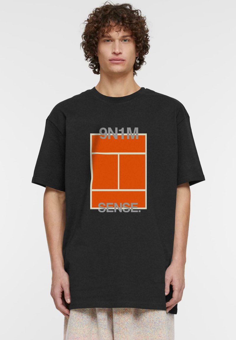Juoda per didelė marškiniai su oranžiniu grafiniu dizainu, kuriame yra tekstas "9N1M" ir "SENSE." Įprasta medvilnės medžiaga su minkštos tekstūros.