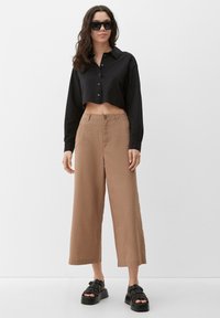 Zwarte cropped button-up shirt, beige wijde broek, en zwarte chunky sandalen. Soepele stof en minimale details.