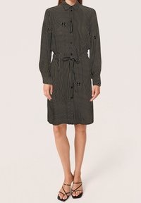 Abito nero a camicia con motivi a linee verticali e geometriche, maniche lunghe, vita con cintura e colletto.