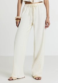 Pantaloni a gamba larga in morbido tessuto crema testurizzato con un elastico in vita e decorazioni floreali ricamate vicino all'orlo.