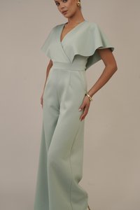 Macaquinho verde menta claro com um design evasé, mangas em forma de flauta e uma cintura ajustada. Apresenta uma textura suave e bolsos laterais. Acessório de bracelete dourado.