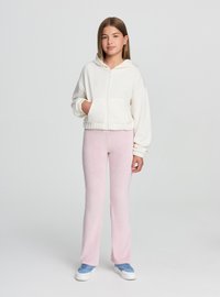 Biała krótka bluza z kapturem zapinana na zamek z elastycznym dołem, zestawiona z jasnoróżowymi rozkloszowanymi spodniami. Niebieskie trampki dopełniają strój.