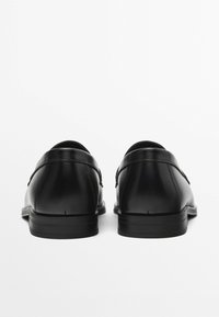Schwarze Lederschuhe mit runden Zehen, glatter Textur und minimalistischem Design. Sie verfügen über einen niedrigen Absatz und kontrastierende Nähte entlang der Nähte.