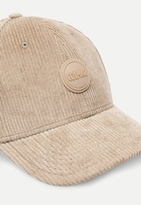 Bežist korjeerkate baseballi müts, millel on ümar äär ja ringikujuline kreemivärvi logo plaastriga, millel on ees kiri "COLMAR". Tekstuurne pind.