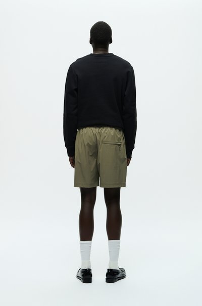 Svart sweatshirt och olivgröna shorts. Shorts har ett elastiskt midjeband och en dragkedjeförsedd bakfick. Vita strumpor och svarta skor avslutar looken.