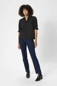 Zwarte kortekoot blouse met knopen en een textuurkraag, gecombineerd met donkerblauwe rechttoe-rechtaan jeans en zwarte enkellaarsjes.
