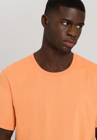 T-shirt arancione a maniche corte realizzato in cotone, con scollatura rotonda e superficie liscia, privo di motivi o loghi.