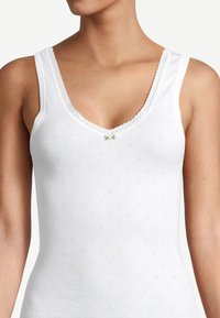 Débardeur blanc avec un décolleté en V et une bordure en dentelle, présentant de petits motifs à œillets et un accent floral délicat au niveau du col.