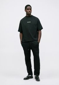 Melnas kokvilnas oversize t-krekls ar nelielu logotipu, kombinēts ar melnām sporta biksēm. Apģērbu papildina melni ādas apavi.