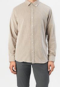 Beżowa koszula z korduroyu z zapięciem na guziki, długimi rękawami i wywiniętym kołnierzykiem. Posiada teksturowany materiał z subtelnymi pionowymi paskami.