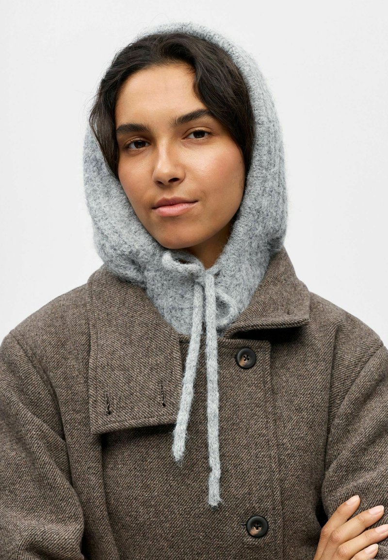 Abrigo de lana marrón con un acabado texturizado, que cuenta con una capucha de punto gris atada en el cuello con lazos, creando un diseño en capas.