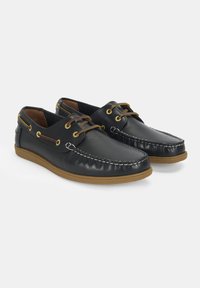 Zwarte leren boot schoenen met een gestructureerde afwerking, contrasterende stiksels, gouden vetertjes en bruine rubberen zolen.