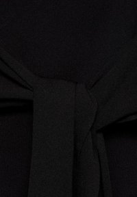 Dettaglio di un indumento in maglia nera con accenti a fiocco. La texture è liscia e il design include un fiocco creato con lo stesso materiale.