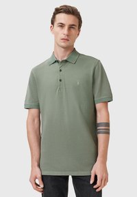 Polo shirt in cotone verde con colletto, abbottonatura a tre bottoni e maniche corte. Presenta un sottile logo ricamato sul petto.