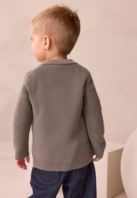 Grau gestrickter Pullover mit geripptem Muster und Kragen, kombiniert mit blauen Jeanshosen. Das Kind ist von hinten zu sehen.