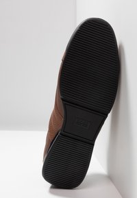 Chaussure en cuir marron avec un design texturé, dotée d'une semelle en caoutchouc noire durable avec une adhérence à motifs et un logo de marque embossé.