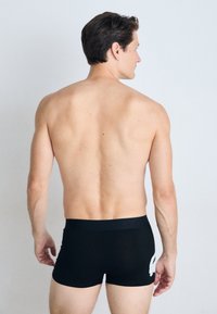 Zwarte boxershorts met een gladde textuur en een elastische tailleband, voorzien van een subtiele witte grafische detail aan de zijkant.