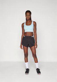 Top desportivo azul claro, calções pretos, detalhe branco, meias brancas, sapatilhas desportivas pretas com detalhes rosa. Design simples, ajuste funcional.