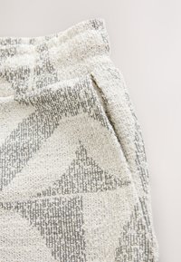 Tkany materiał w kolorze ecru z szarymi geometrycznymi wzorami, posiadający lekko plisowany pas oraz miękką, włóczkową fakturę.