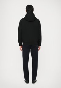 Svart hettegenser med stor hette, ribbede mansjetter og kant, kombinert med mørk marinebukser. Glatt stoff, minimalistisk design, ingen synlige logoer.