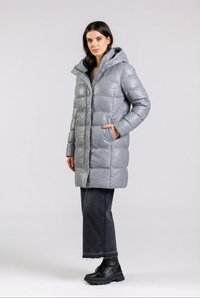 Kvinde stående iført en hættetrøje, lang grå dunjakke, sorte beskårne vidde-jeans og sorte snørestøvler med plateau.