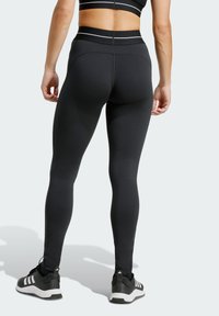 Black athletic leggings with a high waist, sleek texture, and white horizontal stripes at the waistband, paired with black running shoes.