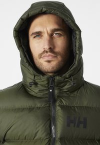 Chaqueta verde esponjosa con capucha, que cuenta con un cierre de cremallera y una marca en negro. El tejido tiene un aspecto brillante y una textura suave.
