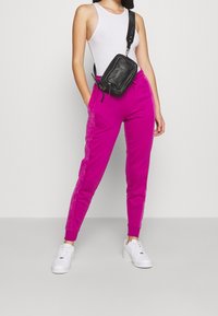 Fuchsia joggingbyxor med ankle cuffs, sidofickor och en slät textur, matchat med en figurnära vit linne och en svart axelväska.