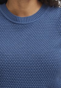 Pletený modrý svetr s texturovaným vzorem a žebrovaným kulatým výstřihem, s hladkým a jemným povrchem.