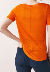 Oranžové tričko s krátkým rukávem a kulatým výstřihem, doplněné o tmavě modré slim fit kalhoty. Hladká textura.