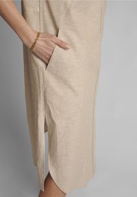Beżowa sukienka z lnu z boczną kieszenią, widocznymi guzikami i rozcięciem na dole. Miękka faktura i casualowy design.