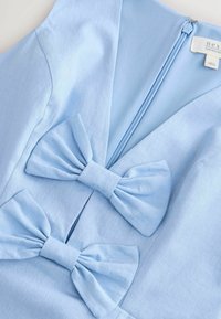 Hellblaues Kleid mit einem V-Ausschnitt, das zwei strukturierte Schleifen auf der Vorderseite und einen verdeckten Reißverschluss auf der Rückseite aufweist.