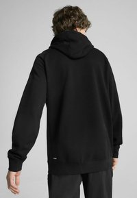 Svart hooded sweatshirt med långa ärmar, en avslappnad passform och ribbade muddarna samt fållen. Har en liten logotagg vid fållen.