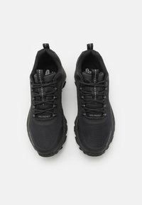 Black athletic shoes with a mesh upper, rounded toe, lace-up design, and textured rubber sole. Features reflective accents and logo detail.