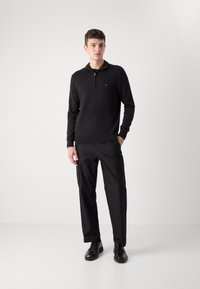 Svart zip-up genser med høy krage, kombinert med svarte cargo-bukser med lommer, båret med svarte snøresko.
