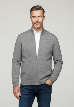 Un sweat à fermeture éclair gris avec un motif de tricot texturé, un col montant et une fermeture à glissière frontale. Assorti à un jean bleu marine.