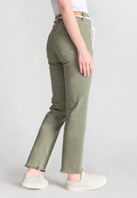 Pantalon taille haute vert olive avec une coupe droite, ourlet effiloché, deux poches arrière avec un design brodé, associé à des baskets blanches.