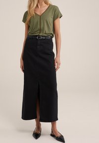 Top verde oliva con cuello en V y mangas cortas, combinado con una falda larga de mezclilla negra que tiene una abertura frontal y un cinturón negro con hebilla de metal.
