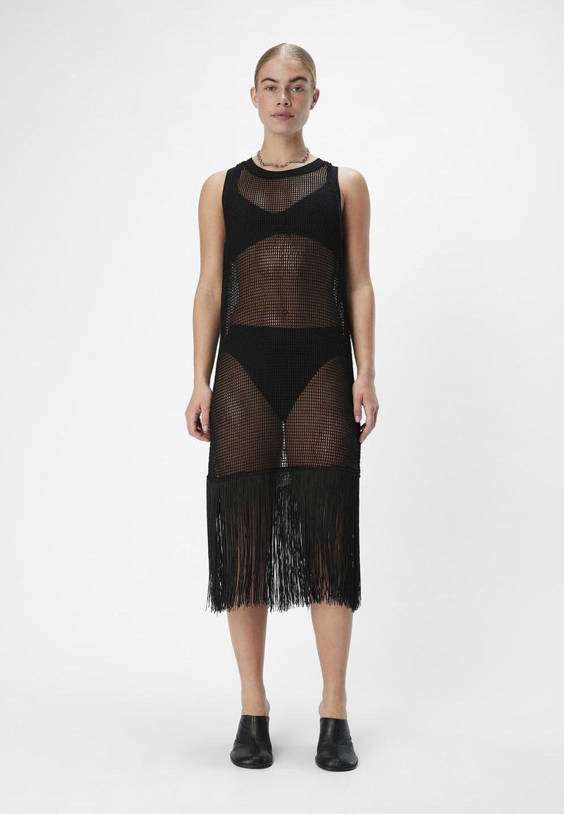 Svart stickad täckkjol med en åtsittande bodice, franskant och genomskinliga sektioner. Bärs över matchande svart bikiniunderdel.