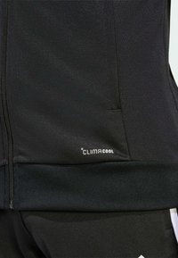 Μαύρο αθλητικό μπουφάν με φερμουάρ, κατασκευασμένο από μαλακό, ελαφρύ ύφασμα και με το λογότυπο CLIMACOOL στο κάτω δεξί μέρος.