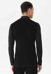 Zwarte longsleeve shirt met een hoge kraag, voorzien van contrasterende grijze gestructureerde mouwen. De materialen lijken glad met minimale naden.